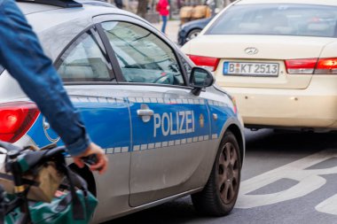 Berlin Almanya - 11 Nisan 2025: Mavi çizgili bir polis arabası kalabalık bir caddede çevresinden geçen araçlar ve yayalar tarafından görüldü.