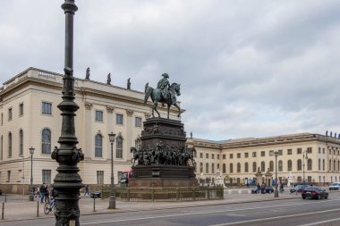 Berlin Almanya - 11 Nisan 2025: Tarihi bir binicilik heykeli eski üniversitenin önündeki meydanda duruyor. İnsanlar bulutlu gökyüzüyle yürür.
