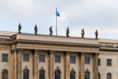 Berlin Almanya - 11 Nisan 2025: Tarihi Humboldt Üniversitesi cephesinde akademik mükemmelliği temsil eden mavi bayrak ve heykellerle süslenmiş klasik mimari sergileniyor.