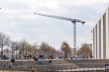 Berlin Almanya - 11 Nisan 2025: Bir inşaat vincinin yoğun bir halk meydanının üzerinde yükseldiği şehir sahnesi.
