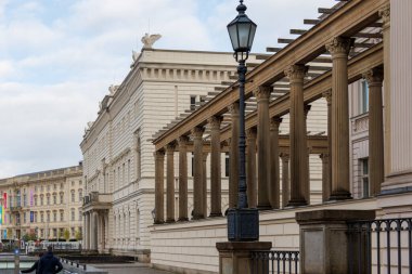 Berlin Almanya - 11 Nisan 2025: Klasik sütunlu tarihi bir binanın mimari görünümü sokak lambası ve bulutlu bir gökyüzü altında kentsel çevre.