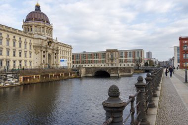 Berlin Almanya - 11 Nisan 2025: Arka planda modern bir yapıya sahip ve yayaların yürüyüş yaptığı tarihi binaların manzarası.
