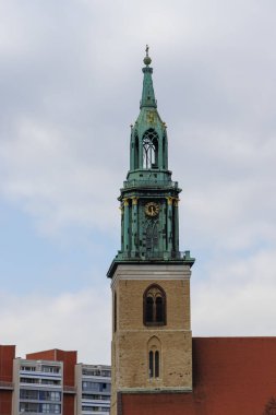 Berlin Almanya - 11 Nisan 2025: Bulutlu gökyüzüne karşı yeşil kuleye sahip tarihi saat kulesi eski ve modern binaları harmanlayan şehir manzarasında mimari zarafet sergiliyor.