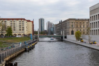 Berlin Almanya - 11 Nisan 2025: Spree Nehri manzarası kentsel arazide yüzen tekneli modern ve tarihi binalarla çevrili.