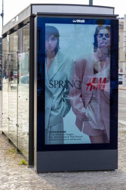 Berlin Almanya - 11 Nisan 2025: H & M için canlı bir ilkbahar reklamı sunan otobüs durağı modern kıyafetlerde kentsel estetiği geliştiren şık modeller sergiliyor.