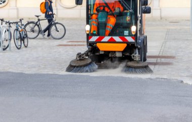 Berlin Almanya - 11 Nisan 2025: Sokak temizleme makinesi kaldırım taşı caddelerini temizlerken bisikletçiler gündüz gözüyle kentsel bakımı sergiliyorlar.