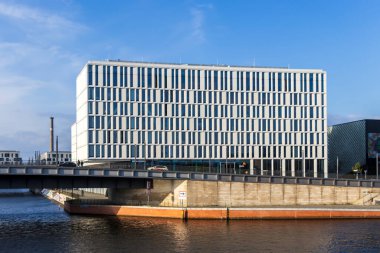 Berlin Almanya - 11 Nisan 2025: Şehir ortamında çağdaş mimari sergilenen mavi gökyüzü altında cam cepheli modern ofis binası.