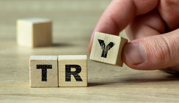 Close-up of a hand holding a wooden letter block to form the word 'TRY' against a soft background symbolizing motivation and persistence in personal goals.