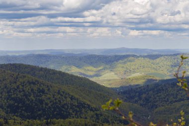 Bieszczady Dağları 'nın çarpıcı manzarası bulutlarla dolu dramatik bir gökyüzünün altında yemyeşil tepeler sergiliyor. İlkbaharda yakalanan bu sahne huzuru ve doğal güzelliği çağrıştırıyor..
