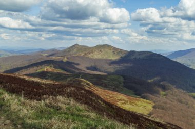 Polonya 'daki Bieszczady Dağları' nın manzarası. Parlak bulutlu bir gökyüzü altında hareketli tepeler ve canlı yeşillikler var. Seyahat ve doğa temaları için ideal.