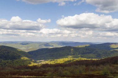 Bieszczady dağlarının nefes kesen manzarası, parlak mavi gökyüzünün altında, kabarık bulutlarla kaplı, yemyeşil tepeleri sergiliyor..