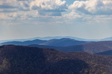 Bieszczady dağlarının panoramik manzarası. Dağınık bulutlar, yemyeşil ağaçlar ve yuvarlanan tepeler, doğa meraklıları ve seyahat promosyonları için mükemmel..