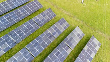 Yeşil bir alana kurulmuş güneş panellerinin hava görüntüsü yenilenebilir enerji teknolojisini ve temiz enerji üretimi için sürdürülebilir uygulamaları gösteriyor.