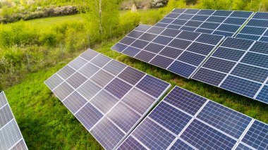 Güneşli bir günde yenilenebilir enerjiyi kullanan yemyeşil bir alandaki güneş panellerinin hava görüntüsü sürdürülebilir teknoloji ve çevre dostu uygulamalar sergiliyor..