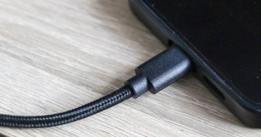 Ahşap bir yüzey üzerinde duran akıllı telefona bağlı siyah bir kabloya yakın çekim. Kablo dayanıklılık ve tarz için örülmüş bir tasarım içerir.