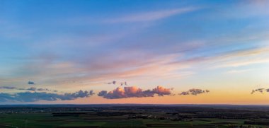 Gün batımında manzaranın göz kamaştırıcı panoramik görüntüsü bulutlarla dolu renkli bir gökyüzünü sergiliyor dingin bir atmosfer ve doğal güzellikle vurgulanmış tarım arazilerine karşı..