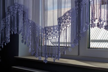 Parlak bir pencereden sarkan zarif dantel perde içeride zarif bir atmosfer yaratıyor. Doğal ışık kumaştan süzülerek karmaşık desenleri ve dokuları güçlendirir..