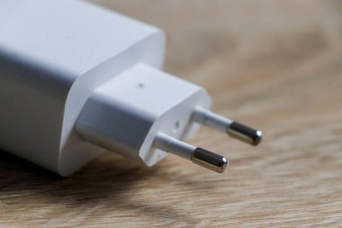 Ahşap bir yüzeye takılı beyaz elektrik şarj aletinin yakın plan görüntüleri teknoloji ve ev teması için ideal metalik iğneler ve parlak tasarımı vurguluyor..