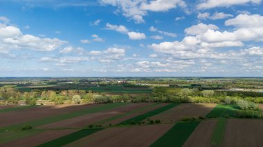 Bereketli yeşil tarlaların ve açık mavi gökyüzünün altında dağınık bulutların altında tarım arazilerinin havadan görünüşü. Manzara canlı bir tarım alanı sergiliyor..