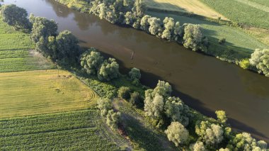 Bereketli yeşil tarlalar ve ağaçlar arasında süzülen sakin bir nehrin havadan görünüşü kırsal bir arazide gün boyunca doğanın güzelliğini yakalıyor..