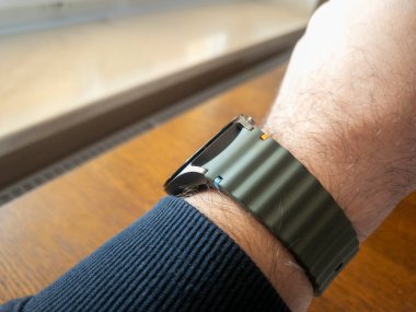 Benzersiz bir tasarımı olan modern bir saat takan bir adamın bileğinin yakın çekimi. Fotoğraf, moda veya yaşam tarzı temaları için ideal bir ahşap masa arkaplanı sergiliyor.