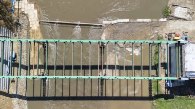 İnşaat işçileri, nehir üzerinde inşaat halindeki yeşil çelik bir köprüde görülebiliyorlar. Hava görüntüsü, güneşli bir günde çalışmanın ilerlemesini yakalar..