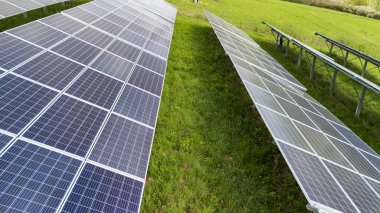 Yenilenebilir enerji teknolojisini gösteren yeşil bir alana kurulmuş güneş panellerinin hava görüntüsü. Paneller, sürdürülebilir uygulamaları destekleyen güneş ışığını yansıtıyor.