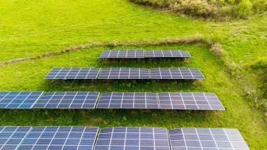 Yeşil bir alana kurulmuş güneş panellerinin hava görüntüsü sürdürülebilir enerji teknolojisini gösteriyor. Canlı otlar, yenilenebilir enerjideki yenilikleri vurgulayan karanlık panellerle çelişiyor..