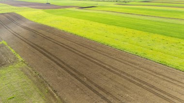 Canlı tarım alanlarının havadan görünüşü taze toprak ve lastik izleriyle yeşil ve kahverengi desenleri gösteriyor. Çiftçilik ve çevresel sürdürülebilirlik kavramları için ideal.