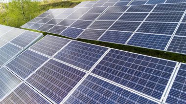 Sıraya dizilmiş güneş panellerinin hava görüntüsü yeşil bir ortamda güneş ışığını yakalıyor. Bu resim yenilenebilir enerji üretimini ve sürdürülebilir teknolojiyi gösteriyor.