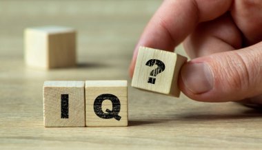 Zekâ ve bilişsel değerlendirmeyi sembolize eden IQ soru işaretli ahşap bir bloğu doğal ışık ile minimalist bir ortamda tutan bir el..