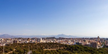Alicante İspanya 'nın panoramik manzarası açık mavi gökyüzü altında kentsel mimari ve uzak dağları gösteriyor. Seyahat ve yaşam tarzı temaları için ideal.