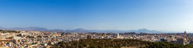 Açık mavi gökyüzü altında yeşil tepeler ve uzak dağların bulunduğu şehir manzaralı Alicante şehrinin panoramik manzarası. Seyahat temaları için ideal.