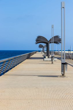 Güneşli bir günde Alicante İspanya 'da dingin bir atmosfer yaratan, okyanusa bakan eşsiz palmiye lambası direkleriyle modern gezinti güvertesi..