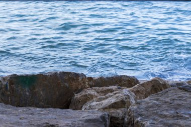 Sakin turkuaz deniz kenarındaki kayalık kıyı şeridi doğal dokuları ve renkleri vurguluyor. Doğanın rahatlığını ve kıyı manzarasını resmetmek için ideal..