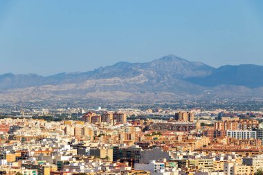 Alicante İspanya 'nın havadan görünüşü Sierra de Aitana dağlarının arka planıyla canlı bir şehir manzarası sergiliyor. Canlı binalar açık bir günde doğal manzarayla harmanlanır..