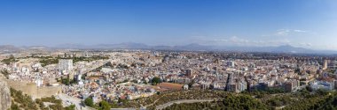 Alicante 'nin panoramik görüntüsü şehir manzarasını, arka planda binalar ve dağlar, seyahat ve şehir hayatı temaları için ideal mavi gökyüzünün altında sergiliyor..