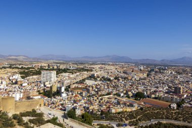 Alicante İspanya 'nın panoramik manzarası, açık mavi bir gökyüzü altında şehrin renkli gökdelenlerini ve etrafındaki dağları gözler önüne seriyor. Seyahat promosyonu için mükemmel.
