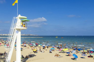 Alicante İspanya - 11 Temmuz 2025: Açık mavi gökyüzü altında güneşlenen güneşlenenlerin ve canlı şemsiyelerin yer aldığı yoğun plaj sahnesi yaz rahatlığının ve eğlencenin özünü yansıtıyor.