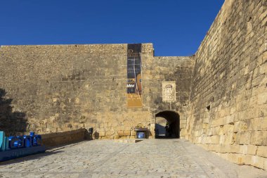 Alicante İspanya - 12 Temmuz 2025: Alicante 'de tanıtım pankartı bulunan tarihi taş duvar. Güneşli bir gün, kaldırım taşı yolunda gölgeler bırakır..