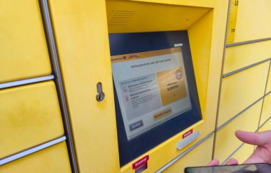 Lahde Almanya - 15 Nisan 2025: Kentsel bir ortamda paket göndermek veya almak için QR kodu tarayan bir kişi DHL paket bırakma kiosku ile etkileşime girdi.