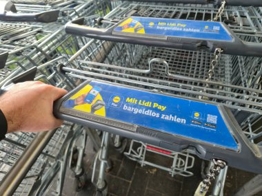 Lahde Almanya - 15 Nisan 2025: Lidl Pay ile bir alışveriş arabasının el ele tutuşması Bir market ortamında modern ödeme metodlarının sergilenmesi.