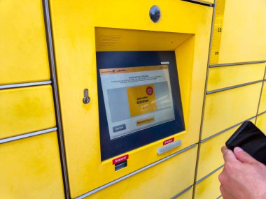 Lahde Almanya - 15 Nisan 2025: Bir kişi DHL paket dolabıyla etkileşime girdi ve modern dağıtım çözümlerini gösteren dijital bir ekran üzerinden bilgi girdi.