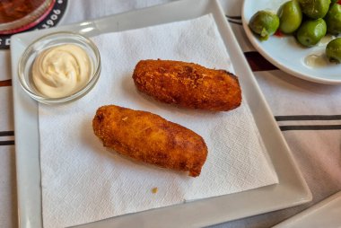 Lezzetli İspanyol kroketleri bir kase mayonezin yanında beyaz tabakta servis ediliyor. Akdeniz restoranlarında aperatifler ya da mezeler için mükemmel..