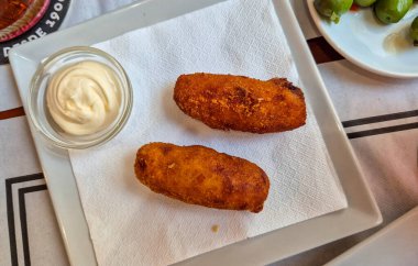 Lezzetli bir tabak İspanyol kroketi basit bir beyaz tabakta kremalı sos ile servis edilir canlı bir yemek ortamında aşçılık deneyimini davet eder..