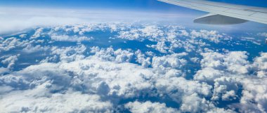 Canlı mavi bir gökyüzü ve seyahat projeleri veya sunumlar için ideal tüylü beyaz bulutlar gösteren bir uçaktan görülen geniş bulutların hava görüntüsü.