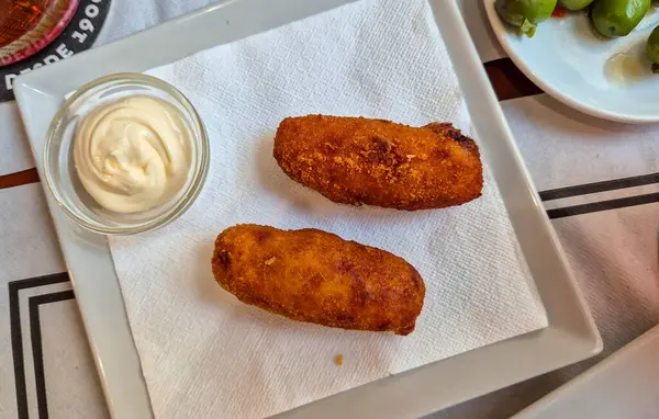 Lezzetli bir tabak İspanyol kroketi basit bir beyaz tabakta kremalı sos ile servis edilir canlı bir yemek ortamında aşçılık deneyimini davet eder..