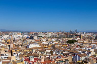 Valencia 'nın canlı bir silueti ve tarihi binaları gösteren hava manzarası. Resim, geleneksel mimari ve modern yapılar arasındaki zıtlığı açık mavi bir gökyüzü altında yakalıyor..