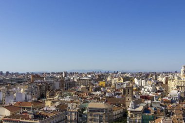 Valencia 'nın panoramik manzarası açık mavi gökyüzü altında çeşitli binalarla güneşli bir günde şehir mimarisi ve canlı çatıları vurguluyor..
