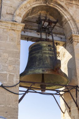 Büyük paslı bir çan taşı bir çan kulesinde asılı açık mavi gökyüzüne karşı. Bu tarihi yapı, huzurlu bir ortamda kültürel mirasın özünü yansıtıyor..